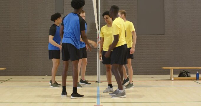 Two opposing adult male teams in blue or yellow shirts walking to net after match, shaking hands