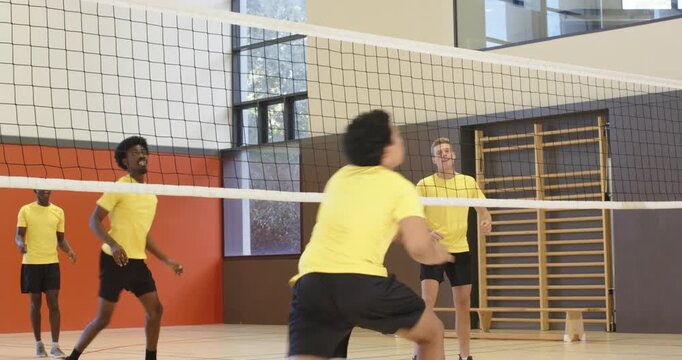Male team in yellow shirts rallying in school gym, ball crossing net, setter placing for score