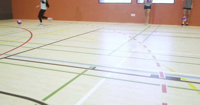 Diverse women practicing drills in gym, one walking from right wall with volleyball, copy space