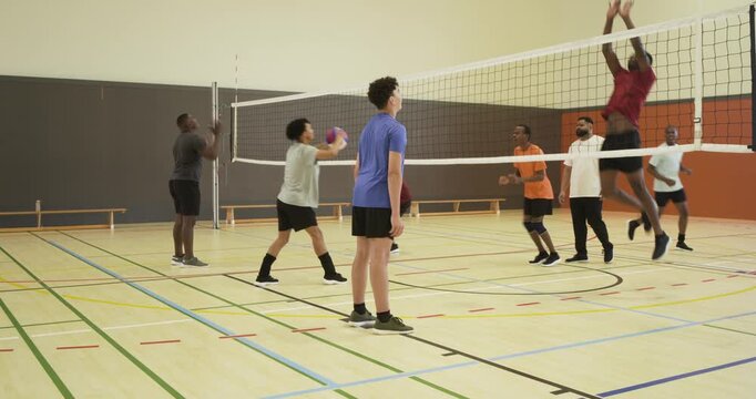 Diverse male volleyball players practicing drill in gym, net and balls, server starting plays