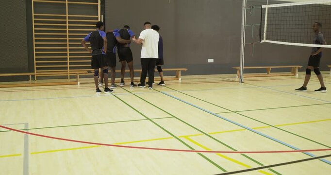 Diverse male volleyball players supporting limping teammate toward bench, crouching inspecting shoe
