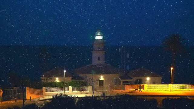The lighthouse is shining by sector lights stands on a cliff on the shores of the Mediterranean Sea in Spain against the night black sky. His ray of light hits the camera and creates beautiful flares