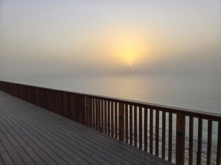 Obraz premium Hazy sunrise over ocean from wooden boardwalk in Tel Aviv