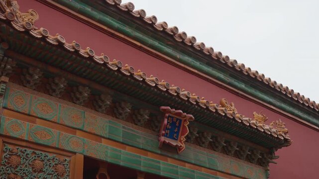 Ornate red gate with green tiles, intricate gilded eaves and painted brackets, enamel plaque with Chinese characters, overcast sky, conservator inspecting faade, heritage tourism and cultural