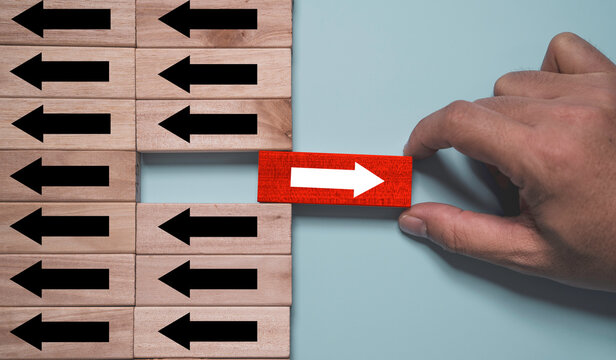 Leadership and innovation concept with hand placing red arrow block opposite direction among black arrows for change management, unique decision making, disruption, differentiation and transformation