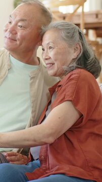 Vertical video: Reaching for cam seniors on sofa leaning, smiling to pose with rust shirt and watch