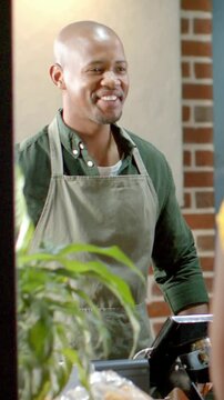 Vertical video: Smiling barista greeting customer approaching POS, wearing green apron at cafe