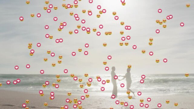 Senior couple holding hands stepping surf, causing heart icons rising, filling sky for marketing