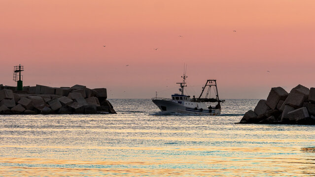 Fishing boat entering Sciacca harbor at sunset
