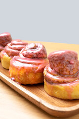 Fototapeta premium Cinnamon rolls with pink glaze on wooden tray