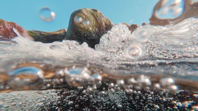 Split-shot perspective: frantic rush of rocky stream with an infinite stream of oxygen bubbles. Slow motion, creating a brilliant, aerated veil beneath surface. Natural underwater scene with torrent