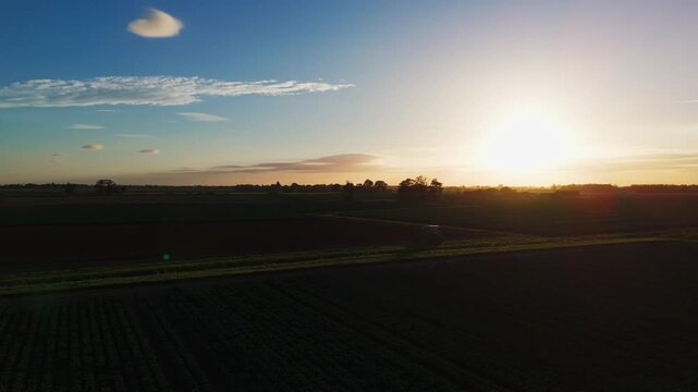 Aerial view of a green tractor plowing a field, cultivating land with a spike tooth harrow cutting, birds in the field looking for food. Summer sunset rural farmland, food production and crop harvest