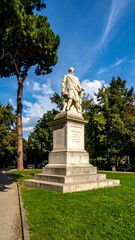 Obraz premium Marble statue on stone pedestal in park setting with tree and blue sky, sunny day