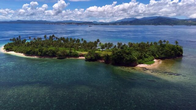 Tilt up aerial reveal of Basul Island showing palm covered shoreline and shallow reef with Surigao City on the horizon