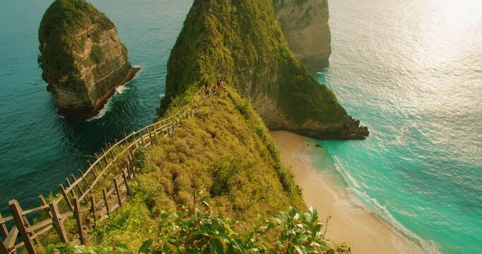 Steep wooden staircase leading down to sandy Kelingking Beach from high green cliff in Bali Nusa Penida