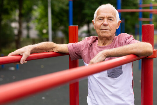 Old man standing between parallel bars outdoors