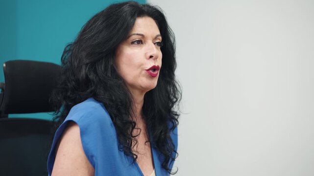 Experienced senior businesswoman with black hair talking and gesturing during a business meeting or interview in a modern office