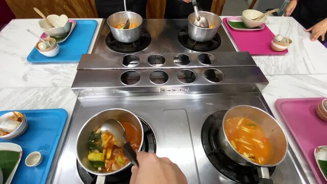 Tom Yum soup being cooked in a restaurant kitchen with fresh herbs and chili, Thai cuisine preparation close-up.