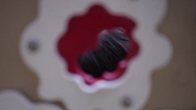 Child peers through a red, flower-shaped hole. Curious eyes blink as she explores the frame. Smiling face shows delight and wonder. Playful moment captured for children's themes