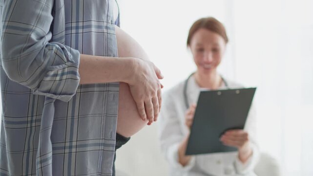 Pregnant woman hands touching big belly in doctor office. Female doctor examining pregnant woman. Gynecologist doctor consulting patient about pregnancy in hospital. Visit to doctor medical checkup