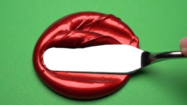 A metallic red substance is being manipulated with a flat tool on a green surface