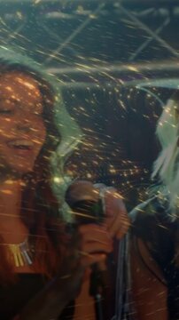 Vertical video: Blonde singer raising hat sparking light trails, duet sharing mic and jamming music