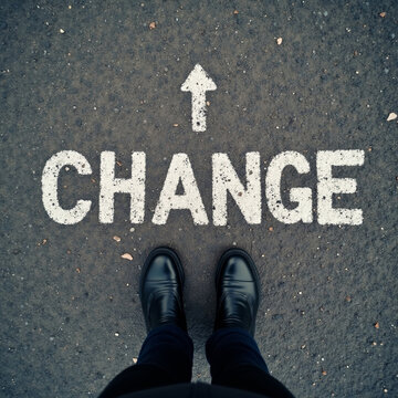 Standing at road word painted CHANGE with arrow pointing forward suggesting point to move and embrace personal change and new direction in life