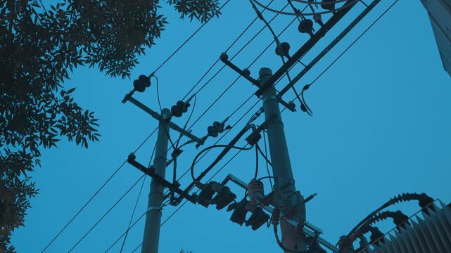 Utility pole transformer cables blue sky highcontrast urban silhouette showing distribution transformer, insulator strings, crossarm, and powerlines weaving through treetop canopy mood cinematic