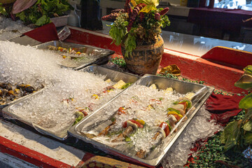 Obraz premium Fresh seafood and vegetable skewers arranged on crushed ice in metal trays at a market display, suggesting freshness, culinary preparation and rustic food presentation with decorative pottery accents.