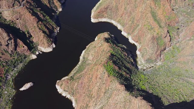Beautiful aerial view of the Parralillo dam in Gran Canaria. The drone flies over the deep blue reservoir winding through a rocky canyon