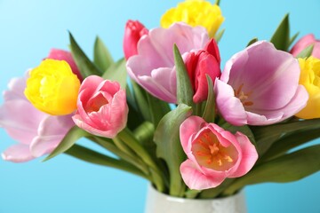 Fototapeta premium Bouquet of colorful tulips in vase on light blue background, closeup