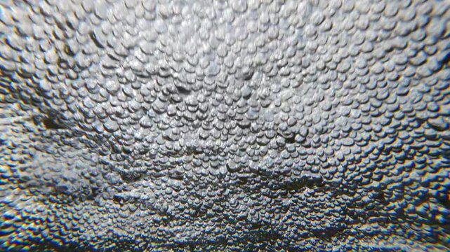 Close-up of air bubbles on water surface swept away by rushing flow downstream of fast river. Rapid movement of aerated, foams water quickly flowing downward, slow motion. 