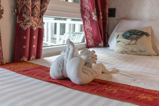 towel swan arranged on a neatly made hotel bed with a red runner and decorative bird pillow, evoking romantic hospitality, luxury accommodation and a welcoming, cozy atmosphere for guests.