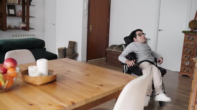 Young man with a physical condition moving in his electric wheelchair to sit at the dining table. Independent living and accessibility at home