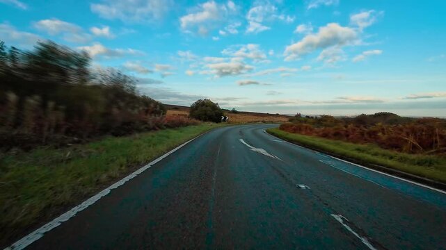 Crossover driving through wet winding road surrounded by autumn fields and trees POV. Automobile moving along countryside highway with patches of sunlight and blue clouds first person view. Car