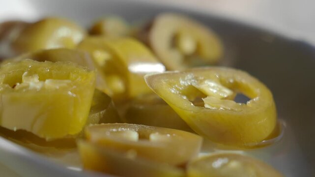 Close up slow motion of fresh pickled green jalape&ntilde;o pepper slices in white bowl.