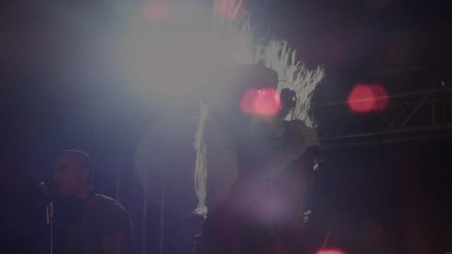 Music driving female singer gripping mic, swaying as backing vocalist harmonizing amid red flares