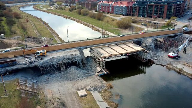 Aerial drone orbit around damaged bridge under construction in Poznan showing repair work, worn structure and urban infrastructure under cloudy sky