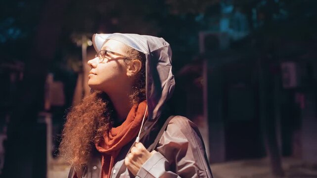Night street portrait young woman backpack roaming historic alley under warm lamps, wearing hoodie and glasses, curly hair cascading, contemplative gaze upward, cinematic bokeh, soft neon highlights,