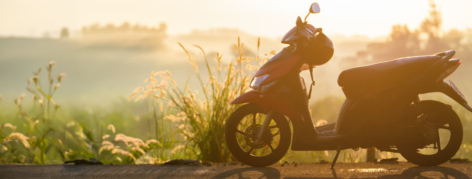 A scooter on an empty road in the morning fog, a symbol of freedom, solo travel, and a slow pace of life in a rural landscape at dawn. Copyspace panorama