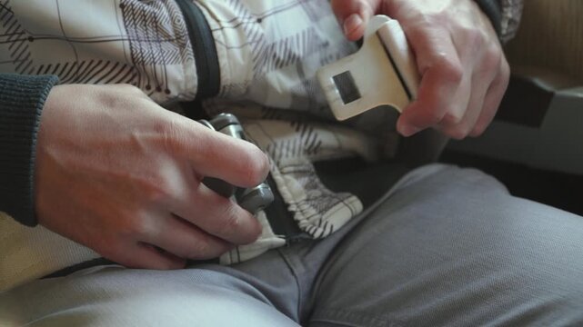Unbuckling of seat belt in airplane seat, close up. Passenger releasing metal buckle of seat belt in airplane cabin after landing. Safe passenger flight.