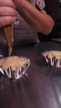A female baker prepares cupcakes using a pastry bag. Vertical video about homemade pastries, cooking and confectionery.