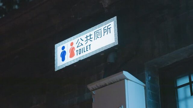 Neon lit public toilet sign at night, mounted on dark building facade with glowing blue and red gender icons, moody urban noir atmosphere, rainslick reflections on metal bracket, cinematic low light,