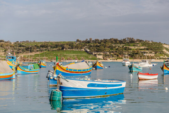 View of vibrant, colorful traditional fishing boats bobbing gently on the tranquil, azure waters reflecting the clear sky, Marsaxlokk, Malta.