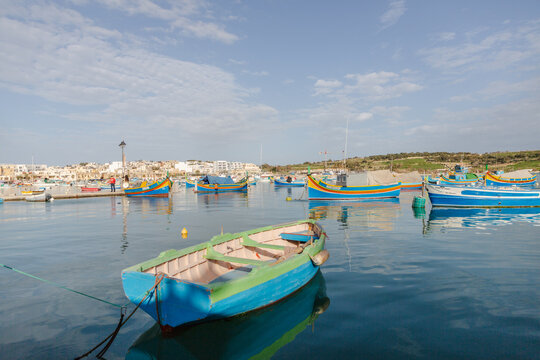 View of vibrant, colorful fishing boats bobbing gently on the tranquil, deep blue harbor waters under a soft sky, Marsaxlokk, Malta.