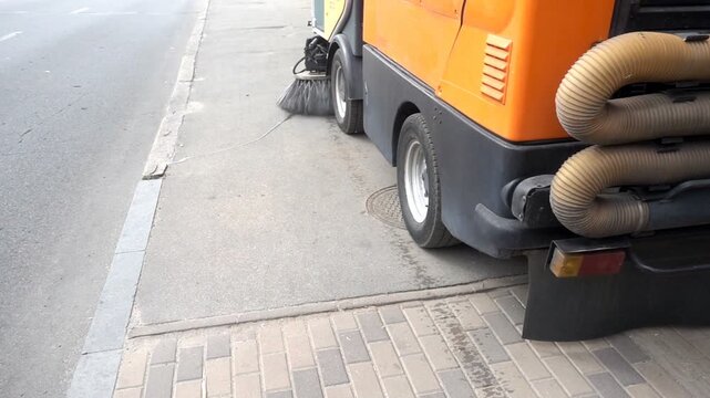 The cleaning machine washes and cleans the sidewalk in slow motion. A city street sweeper cleans the road.