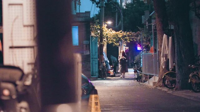 Laneway evening lights pedestrians approaching warmly string garlands glow over sidewalk, candid locals pass by, film grain texture, warm neon and lamppost contrast, nostalgic urban mood