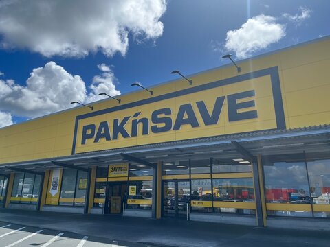 PAK'nSAVE supermarket exterior storefront with iconic yellow signage and entry doors under a blue sky at the Otara-Papatoetoe branch - Auckland, New Zealand, February 8, 2023