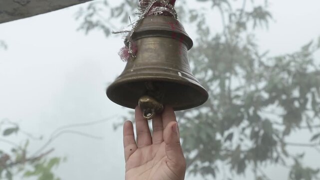 Close view of a hand ringing a traditional temple bell, symbolizing devotion, spirituality, and daily prayer rituals in Indian cultural and religious practices.