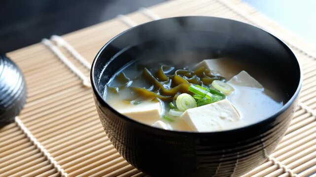 Steaming Bowl of Miso Soup With Tofu and Seaweed on a Bamboo Mat